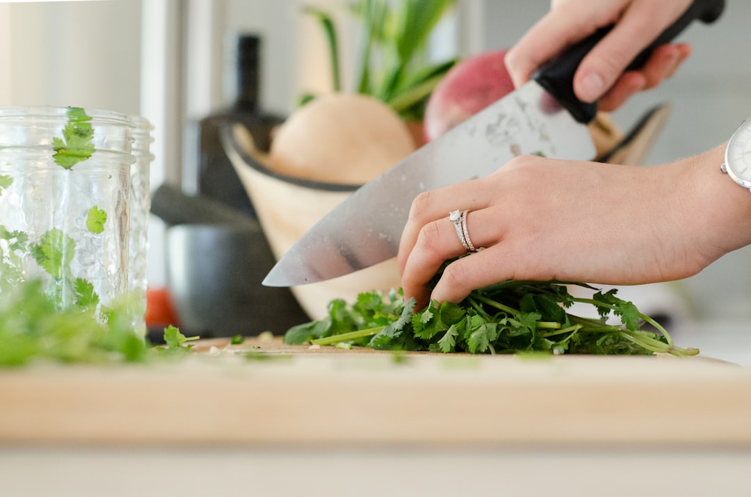 Hands chopping fresh herbs with a sharp chef's knife on a cutting board