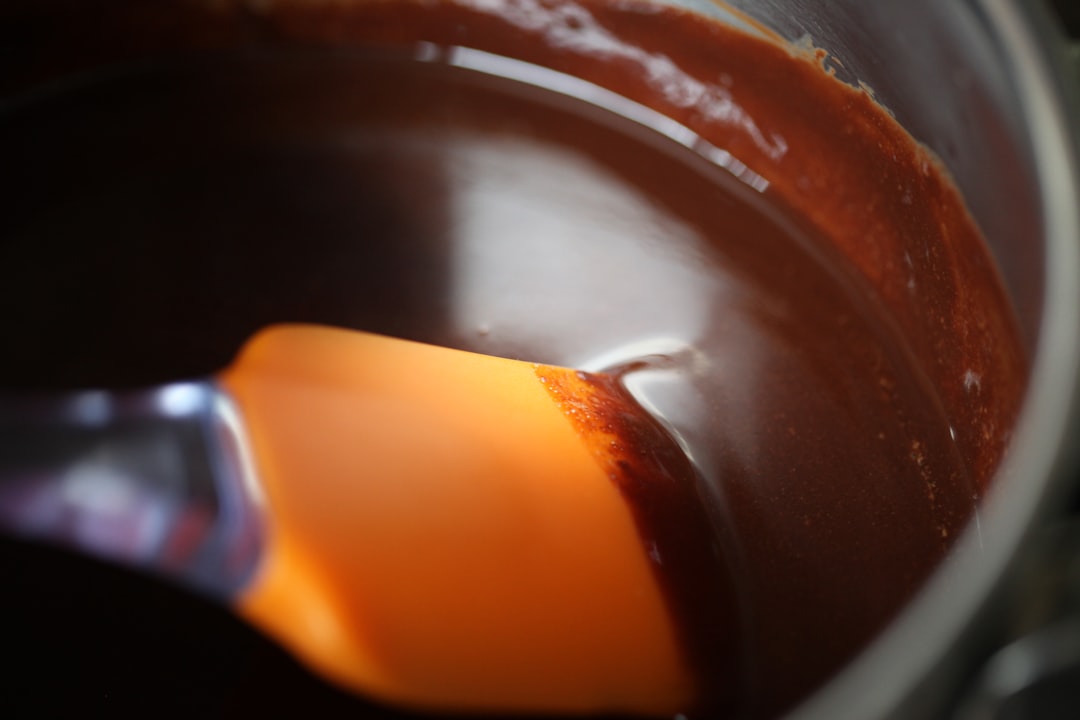 A silicone spatula stirring melted dark chocolate in a saucepan
