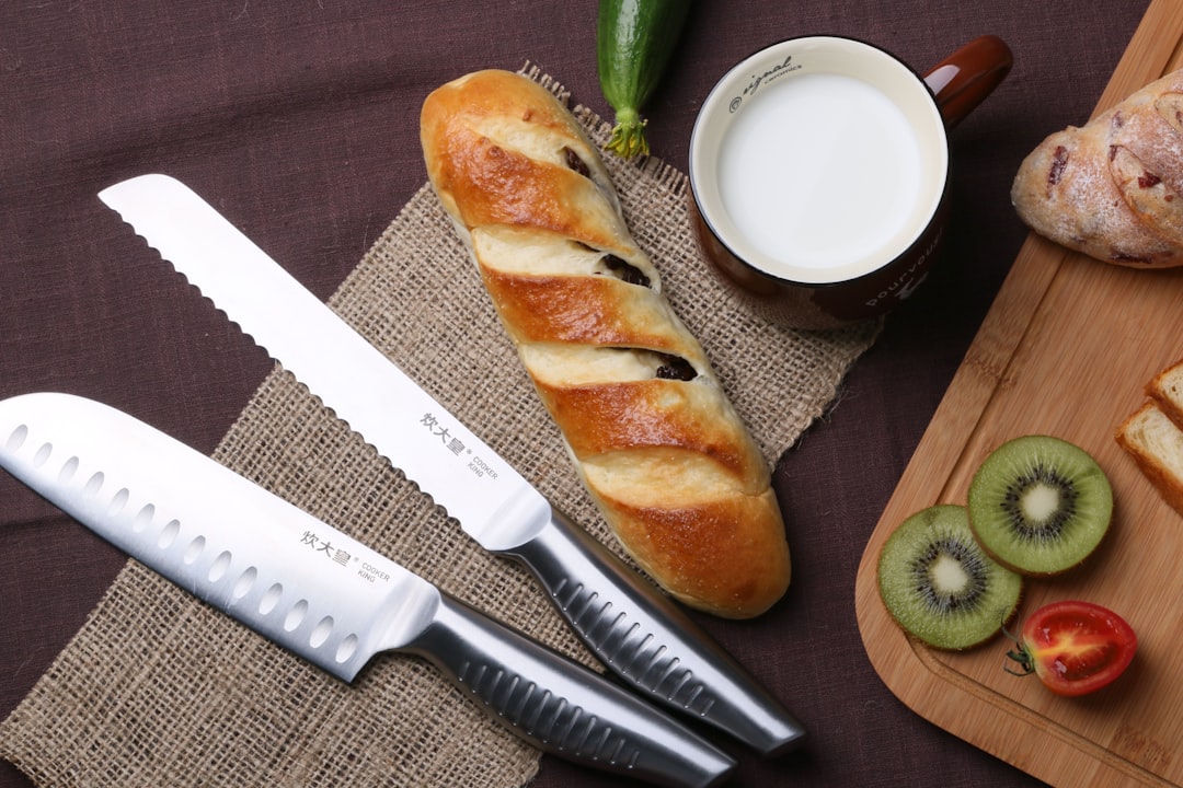 Two chef's knives laid out on a cutting board next to bread, milk, and sliced fruit